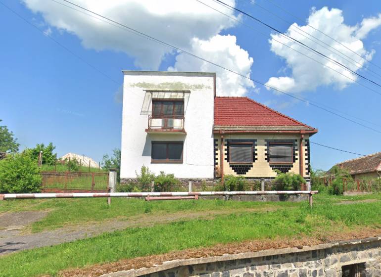 A family house in Nová Bašta with a white facade, a red roof, and a green lawn.