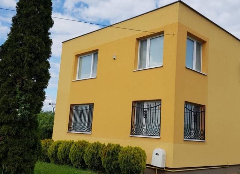 A family house in Stretavka with a striking yellow facade, surrounded by greenery and tall trees.
