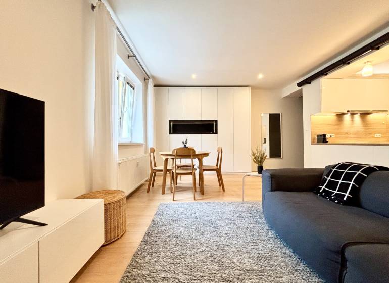Living room with wood-patterned flooring and a kitchenette in a three-room apartment.