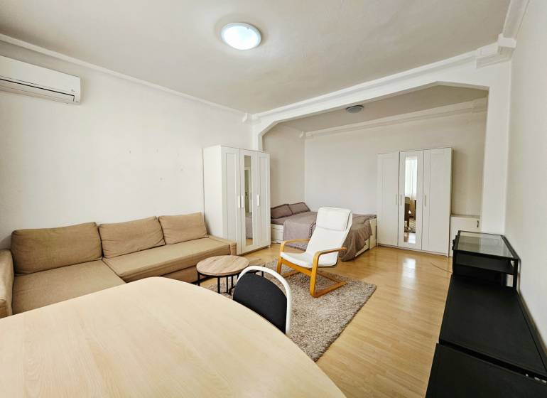 Living room in a two-room apartment with a wooden decor floor and simple furnishings.
