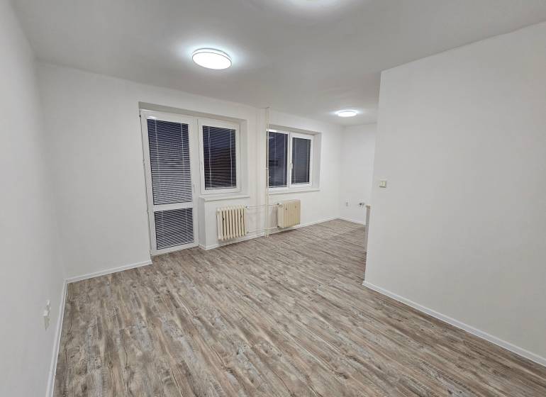An office with white walls and a wooden decor floor, with a window and a radiator.