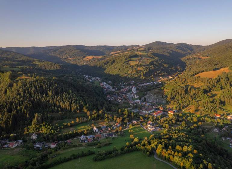 A mountainous landscape with agricultural and forest lands in the village of Lazy pod Makytou at sunset.