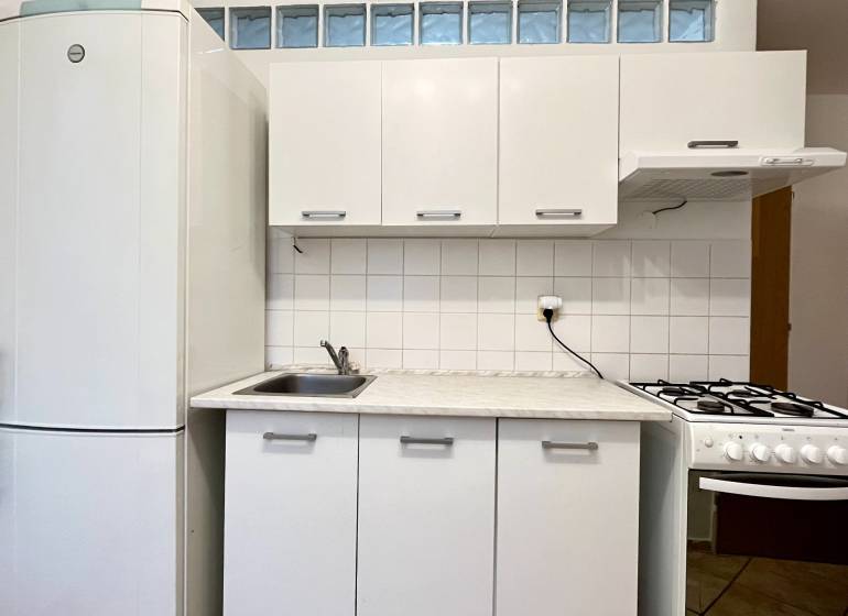 A kitchen with white cabinets and a refrigerator in a studio apartment.