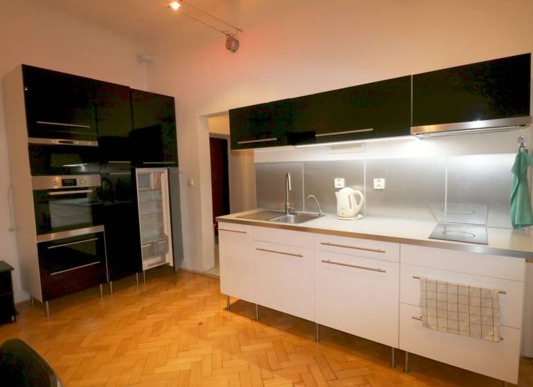 A kitchen in a 3-room apartment with a wood-patterned floor and a black kitchen unit.