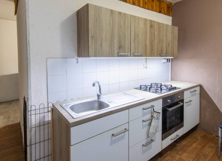 A kitchen with wood-patterned flooring, white tiles, and a gas stove in a 2-room apartment.