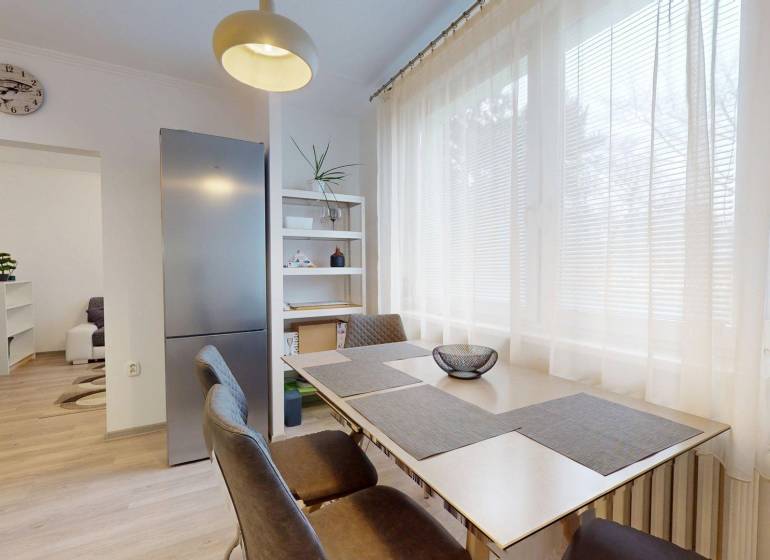 Dining area in a 2-room apartment with a wooden decor floor and light furniture.