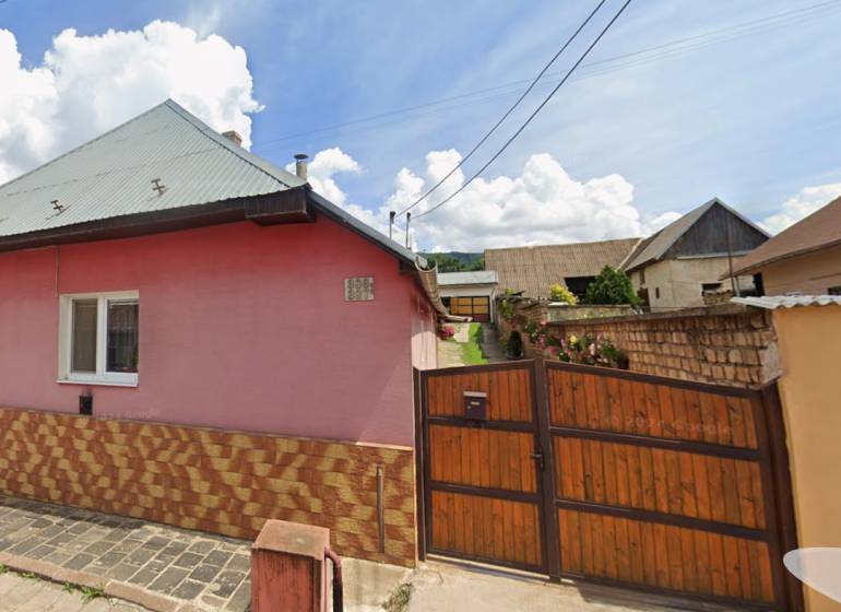 A family house in Jelšava with a pink facade, a sloped roof, and a wooden gate.