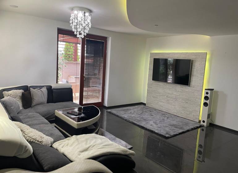 Living room in a family house with a sofa and a television on a wall with stone cladding.