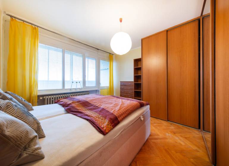 A bright bedroom with a large bed and a wardrobe in a three-room apartment, with a wooden decor floor.