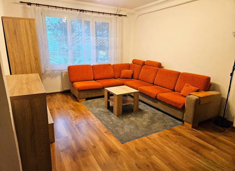 Living room with an orange sofa and wood-patterned flooring in a three-room apartment.