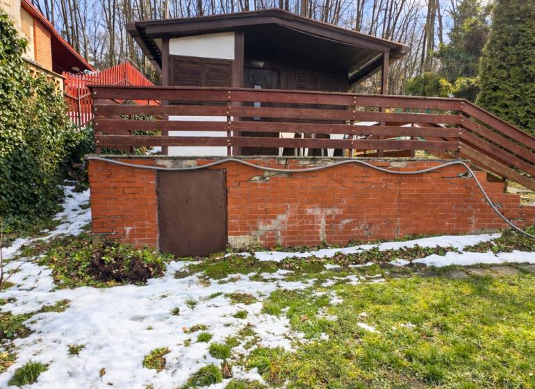 A cottage in Šemša surrounded by greenery and snow, with a terrace and a brick foundation.