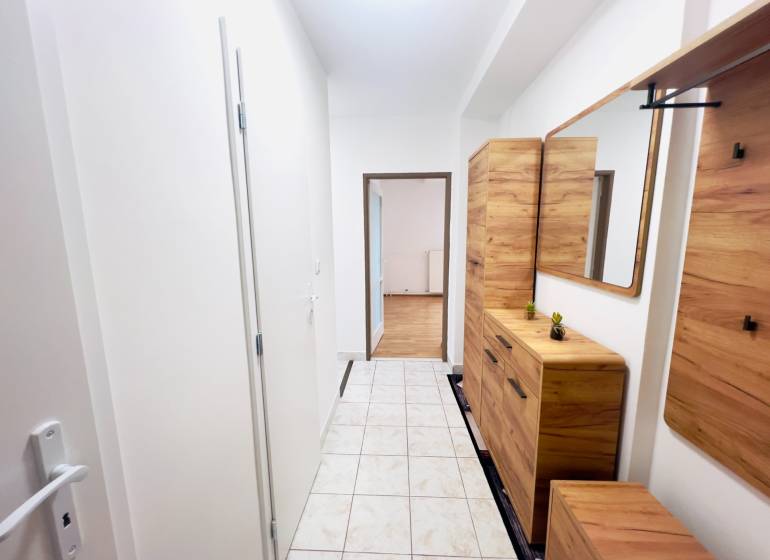 A hallway in a 2-room apartment with tiled flooring and wooden decor furniture.