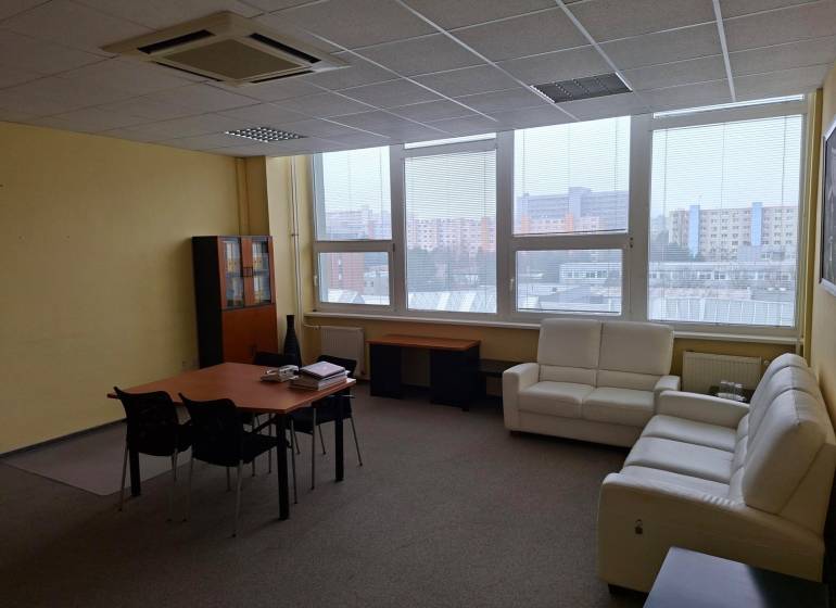 Spacious office with sofas, a desk, and windows overlooking the city skyline.
