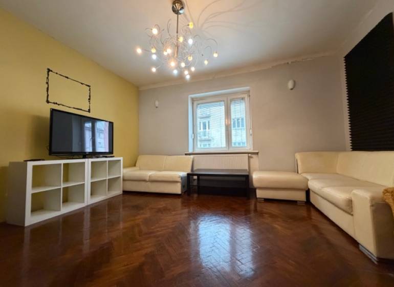 Living room with white sofas, wood-patterned flooring, and a light chandelier in a three-room apartment.