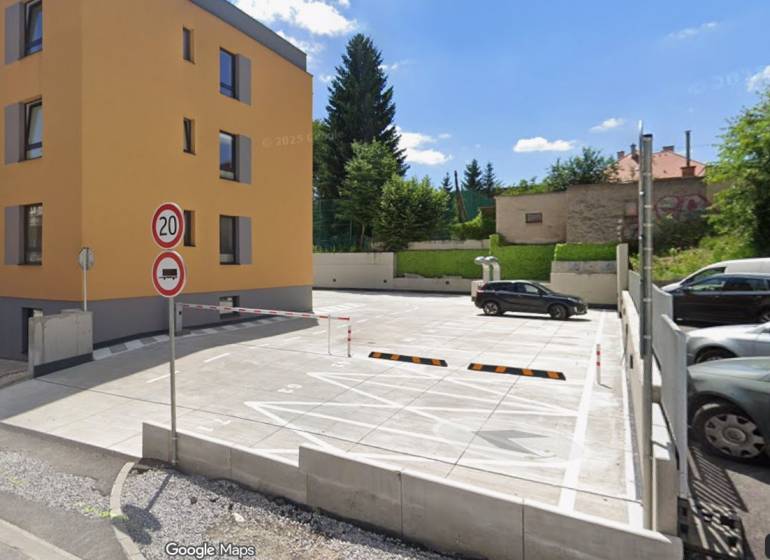 Parking lot and residential building on Rudlovská Road in Banská Bystrica surrounded by greenery.