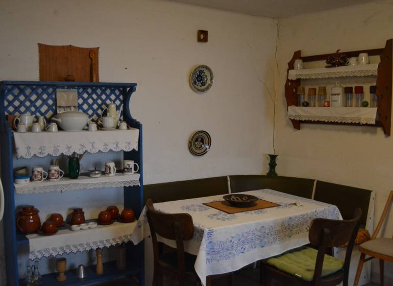 A dining room in a family house with a blue shelf and wooden furniture, decorated with dishes and a tablecloth.