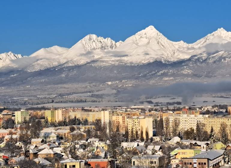 Snow-covered mountains with a view of part of the city of Poprad and multi-story buildings.