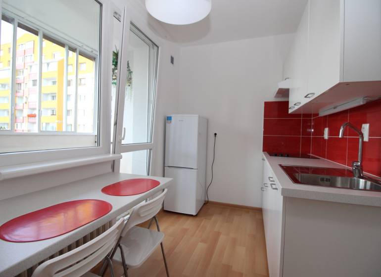 A kitchen in a studio apartment with red tiles, a wood-patterned floor, and a refrigerator.