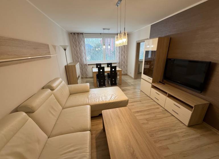 Living room with wood-patterned flooring, a large sofa, and a dining table in a three-room apartment.