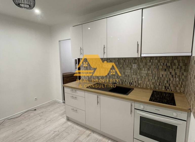A kitchen in a studio apartment with a light-colored kitchen unit and a floor with a wood decor.