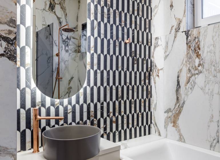 A bathroom with marble tiles, an oval mirror, and a freestanding sink in a 2-room apartment.