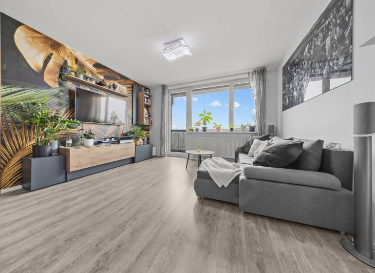 Living room with a comfortable sofa, wallpaper with a plant motif, and a wooden decor floor.