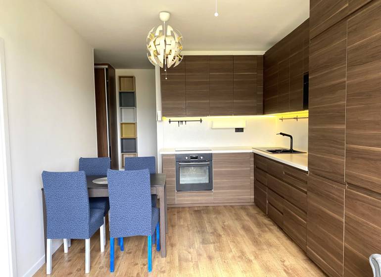A kitchen in a 3-room apartment with a dining table, modern lighting, and a floor with a wooden decor.
