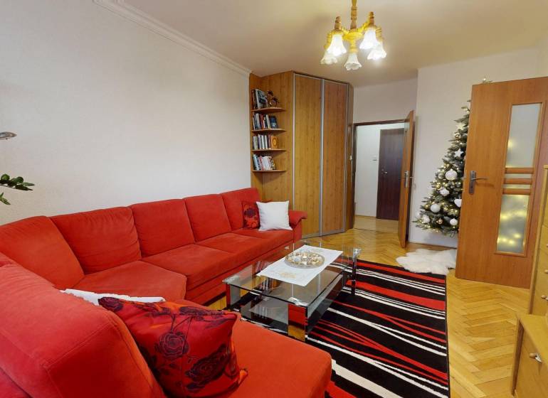 Living room in a 3-room apartment with a red sofa, a fir tree, and a floor with a wooden decor.