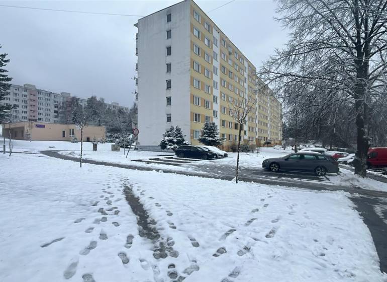 A winter scene on Bazovského Street in Zvolen with an apartment building and parked cars.