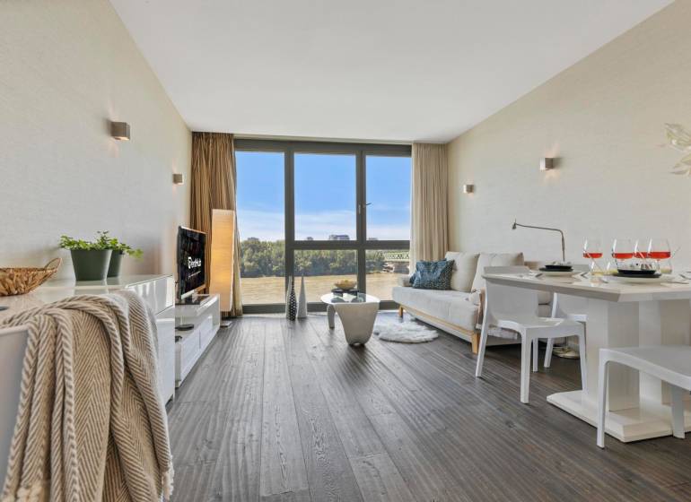 A stylish living room in a two-room apartment with a wooden decor floor and large windows.