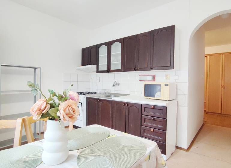 A kitchen in a 2-room apartment with dark cabinets and a dining table with decoration.