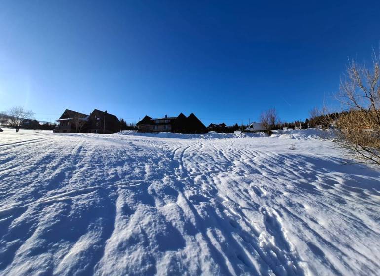 Snow-covered lands in Ždiar with visible houses in the background, clear blue sky.