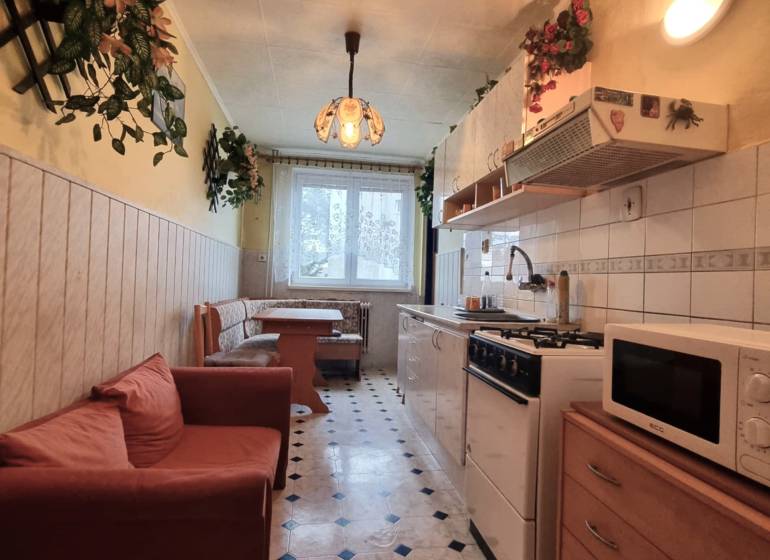 A kitchen in a 3-room apartment with a dining area, a sofa, and a patterned floor.