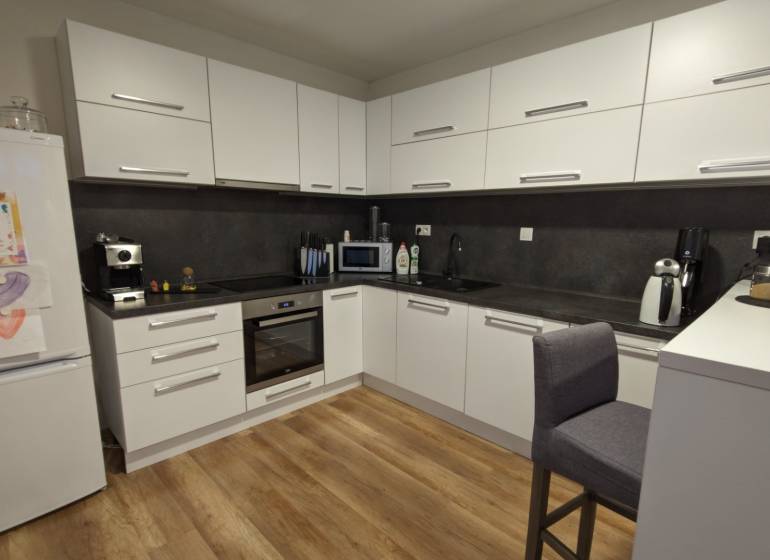 A kitchen in a 2-room apartment with a wood-patterned floor and white cabinets.