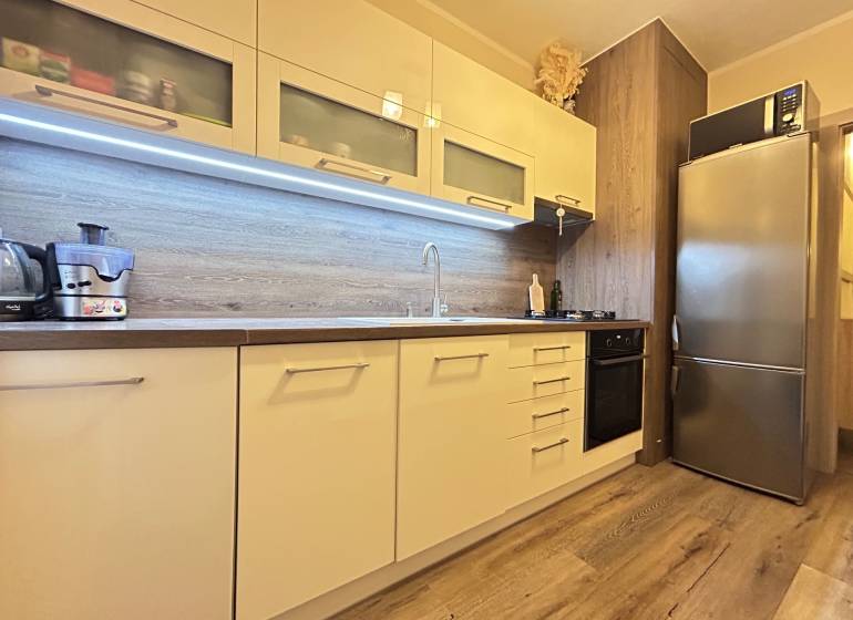 A kitchen in a 2-room apartment with a wooden decor floor, built-in appliances, and storage cabinets.