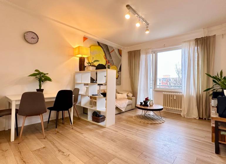 Living room in a two-room apartment with a wooden decor floor and light furniture.