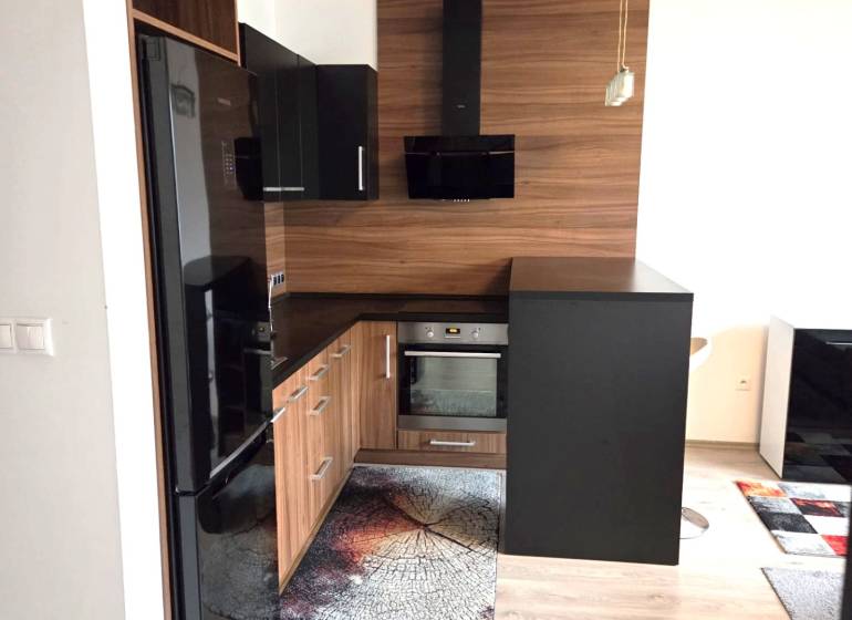 A kitchen in a studio apartment with dark furniture and a wooden decor floor.
