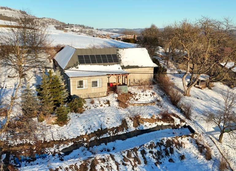 A cottage on Zánemecká Street in Hriňová, surrounded by a snowy hilly landscape with solar panels.