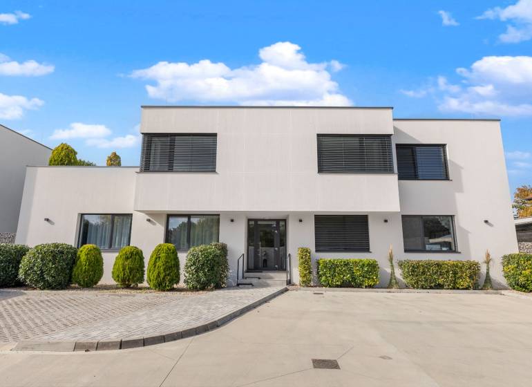 A building with a minimalist design, greenery, and a parking lot on Lipnicka Street in Dunajska Luzna.