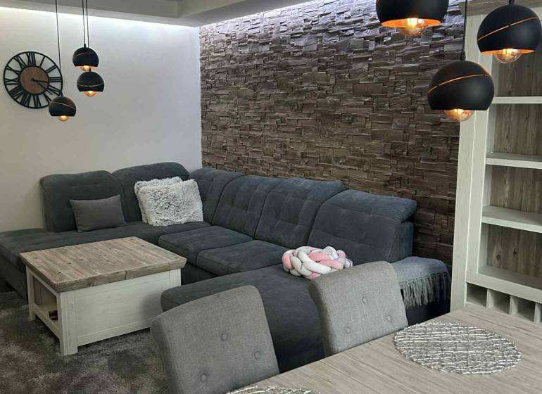 Living room with a corner sofa, hanging lamps, and decorative stone cladding in a 3-room apartment.