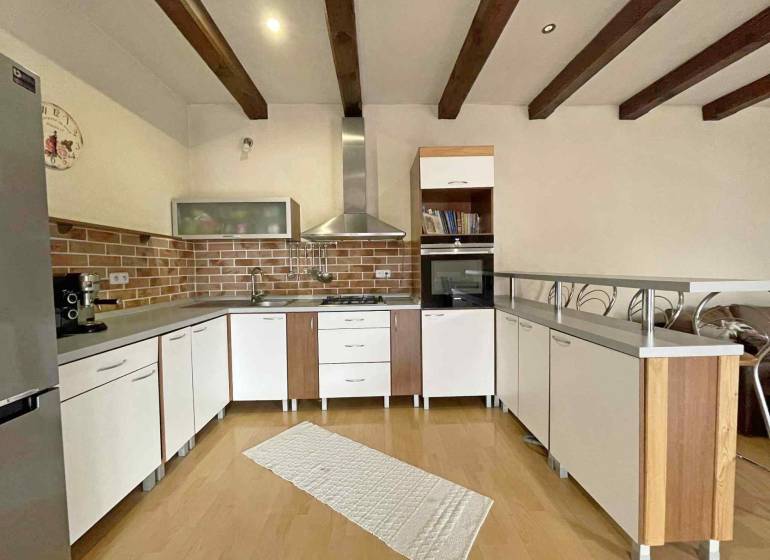 A kitchen in a family house with a wooden decor floor, light furniture, and brick cladding.