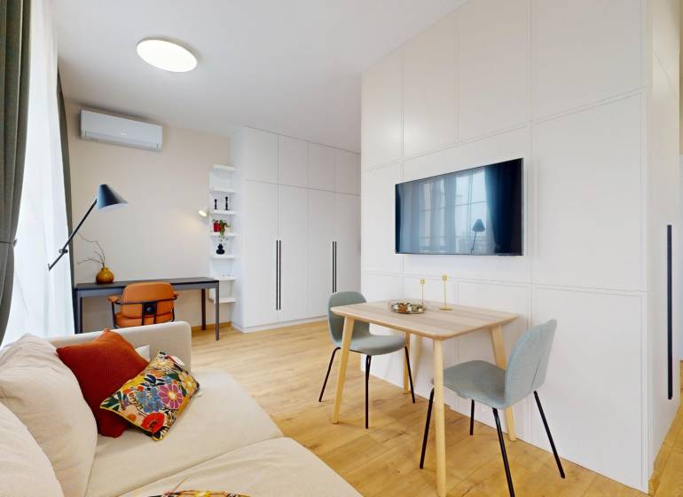 Living room in a one-bedroom apartment with wood-patterned flooring and a desk.