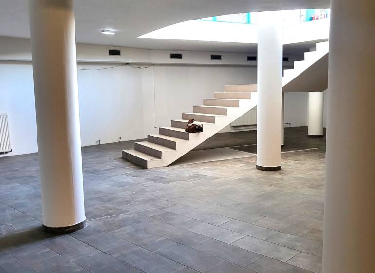 Commercial spaces with marble flooring and staircase, supported by columns.