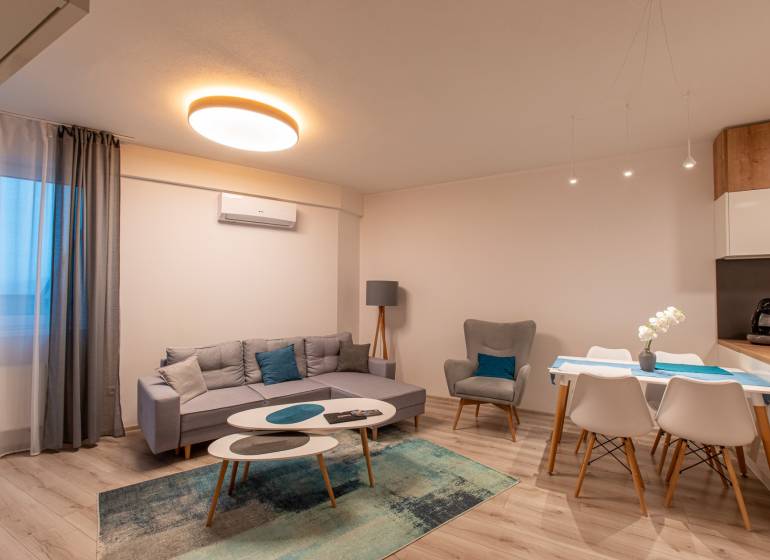 Living room in a two-room apartment with a wooden decor floor, a sofa, and a dining table.