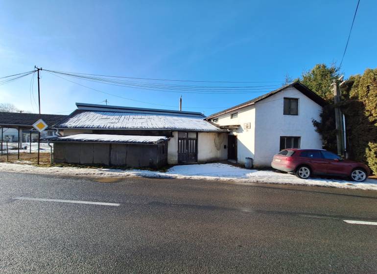 A building by the road with a snow-covered roof and a parked car in Medzany.