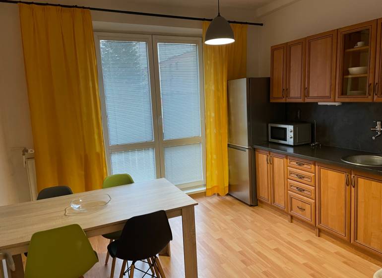 A kitchen in a studio apartment with yellow curtains and a wood-patterned floor.