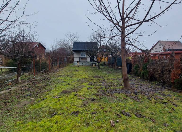A garden with a cottage in Nové Zámky surrounded by trees and a grassy area.