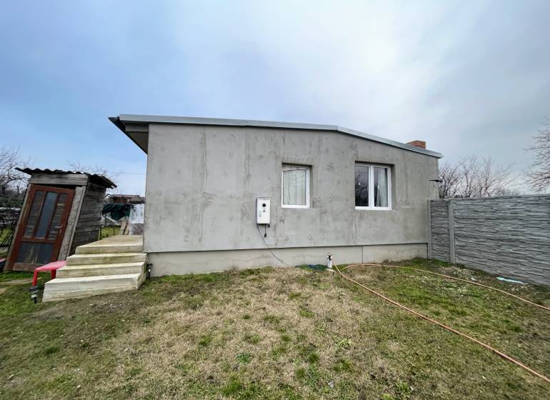 A cottage in Komárno with a concrete facade, stairs, and a fenced plot.