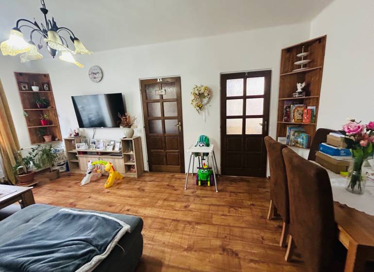 Living room with a sofa, wooden decor flooring, a television, and children's toys in a three-room apartment.