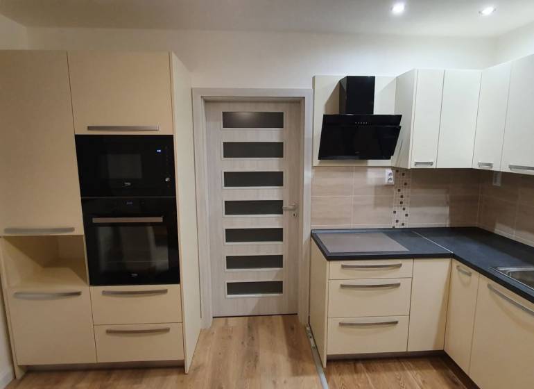 A kitchen in a 2-room apartment with modern cabinets, appliances, and a wooden decor floor.
